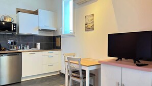 Et kompakt køkken med hvide skabe, en mikroovn, en opvaskemaskine og et spiseområde med et bord og stole.