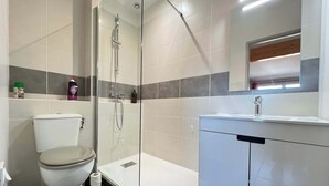 Een moderne badkamer met een douchecabine van glas, een toilet en een wastafelmeubel met een wastafel.