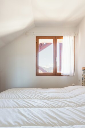Un dormitorio con una cama grande, una ventana con cortinas y vistas a montañas.