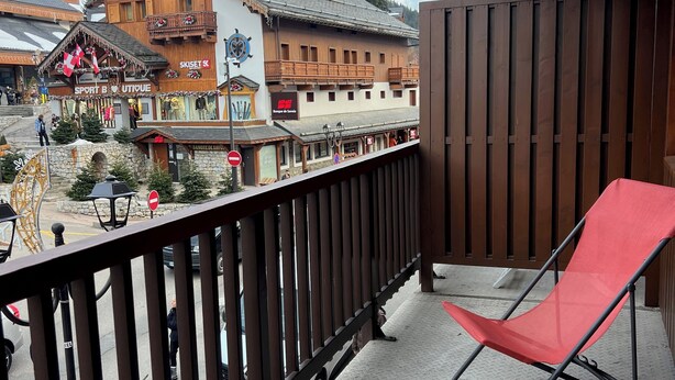 A balcony with a red chair, a view of a ski resort, and traditional wooden buildings. - EXCEPTIONAL PRICE Méribel center ski in ski out with parking ski locker and balcony (meribel)