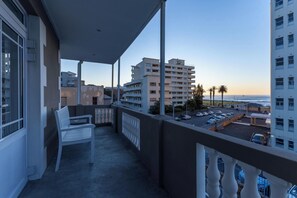 A balcony with a white chair, overlooking a parking area and buildings with a view of the ocean. - Sea Point View 3bed Apartment Cornerstone Place (Cape Town)