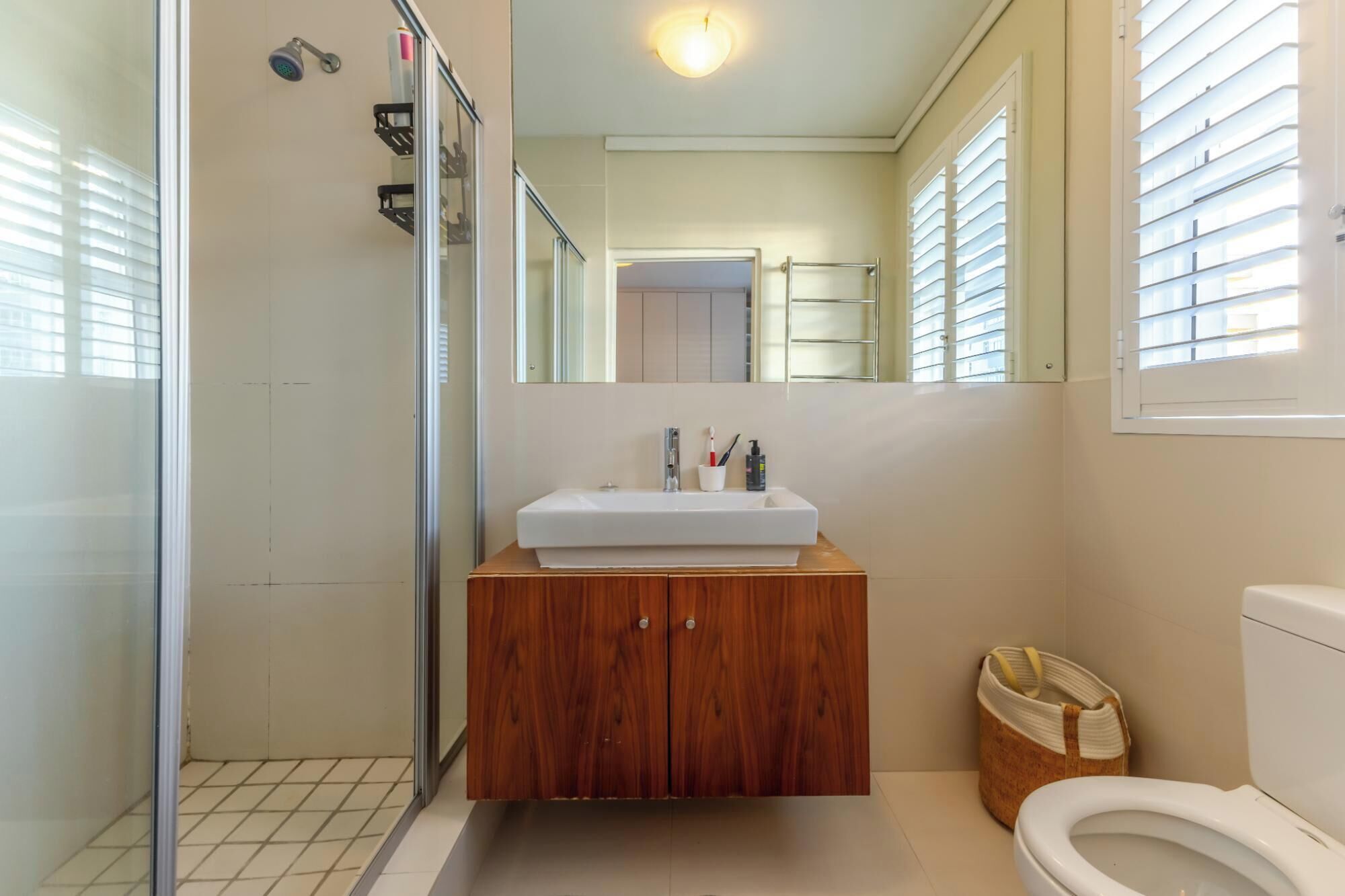 A bathroom with a glass shower enclosure, a white sink with a wooden vanity, and a toilet.