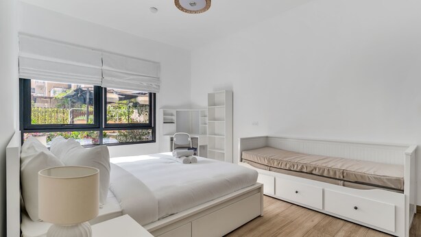 A modern bedroom with a large bed, bedside storage, a desk, and a view of the outdoors. - Stayshort - Warm Spacious 3 Bedroom in The Greens That Sleeps 8 (Dubai)