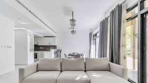 A modern living room with a sectional sofa, a chandelier, and a dining area in the background. - Stayshort - Warm Spacious 3 Bedroom in The Greens That Sleeps 8 (Dubai)