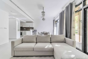A modern living room with a sectional sofa, a chandelier, and a dining area in the background. - Stayshort - Warm Spacious 3 Bedroom in The Greens That Sleeps 8 (Dubai)
