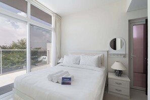 A hotel room with a large bed, a bedside table with a lamp, a mirror, and a view of the outdoors through a balcony. - Stayshort - Modern 3 BR Villa in Damac Hills 2 With Garden That Sleeps 6 (Dubai)