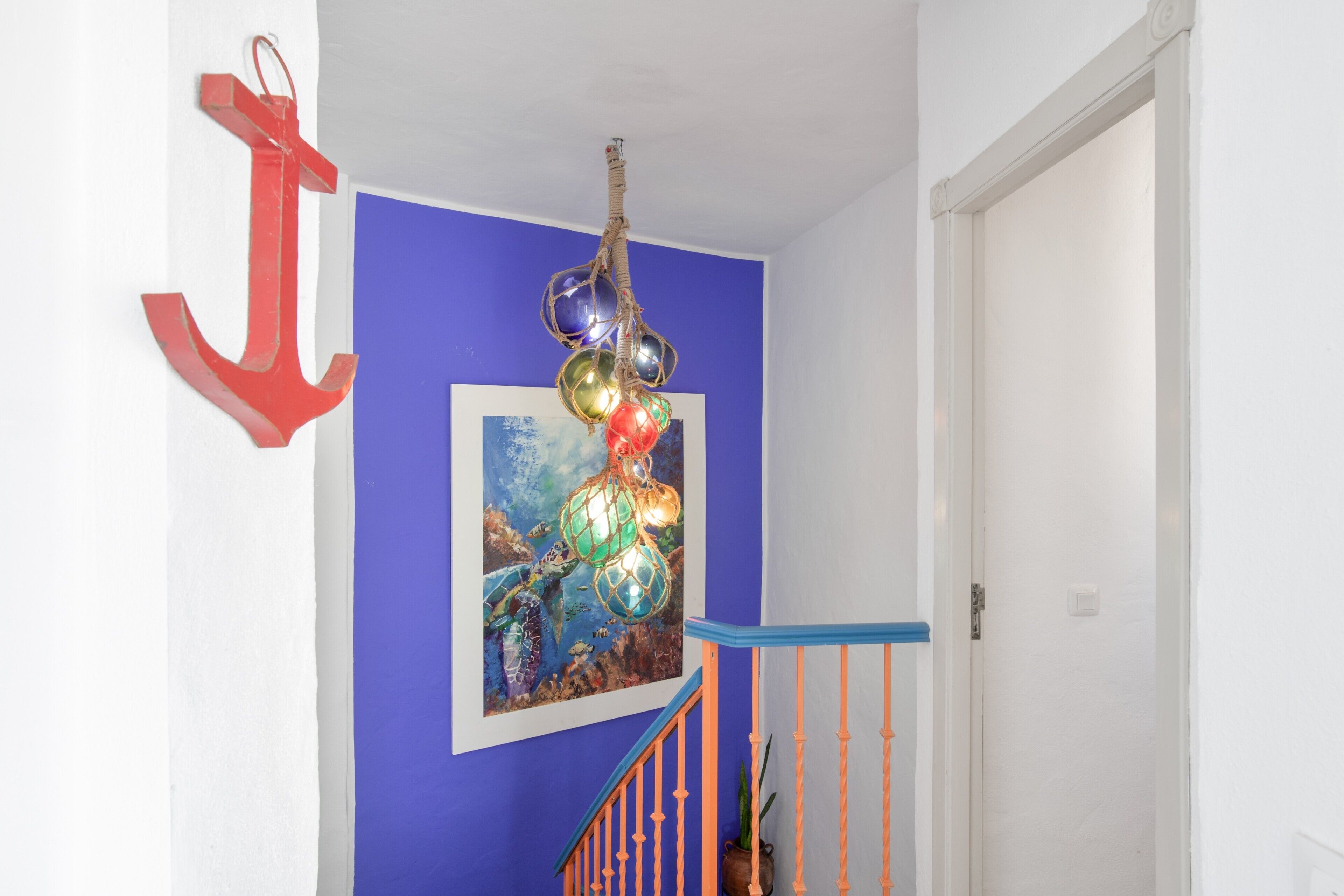 Un escalier avec une rampe bleue, une décoration en forme d’ancre rouge et une peinture abstraite aux couleurs vives sur le mur.