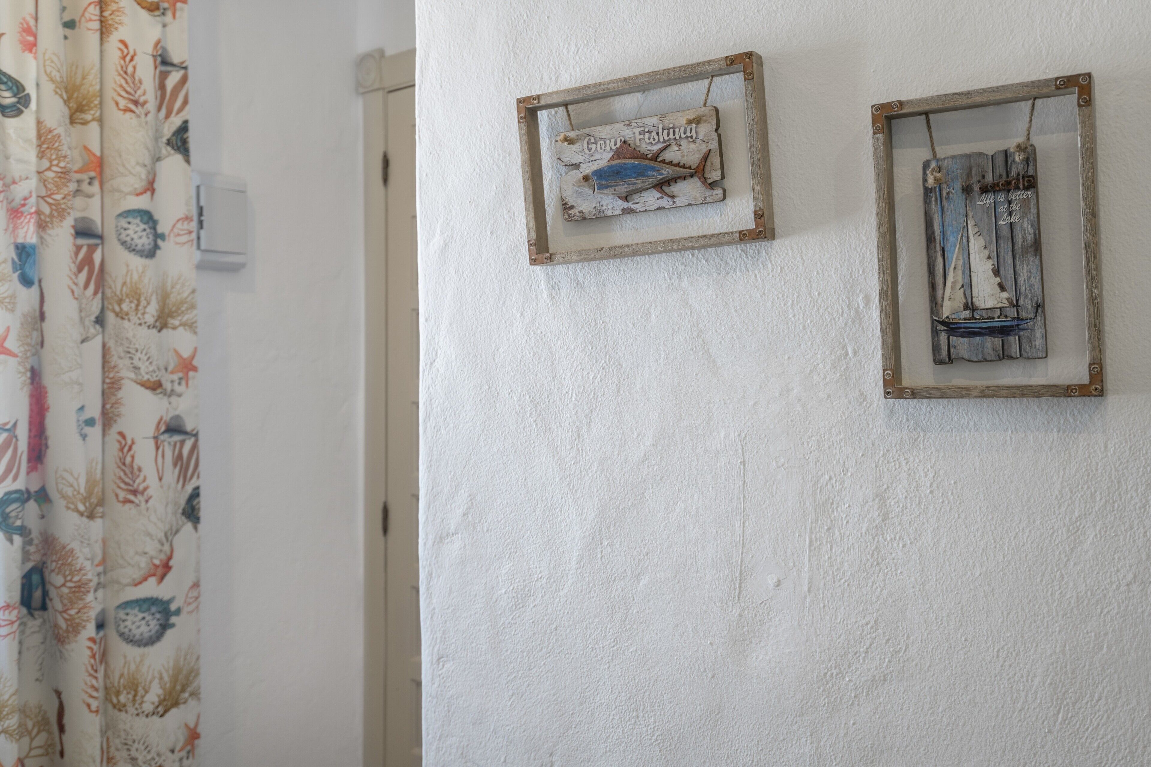 Una pared con dos carteles de madera rústica, uno con la imagen de un pez y otro con una vela, y una cortina con estampado marino.