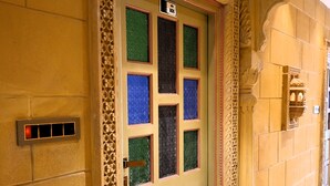 Entrada de un hotel con una puerta decorativa, piso a cuadros y una lámpara fijada a la pared.