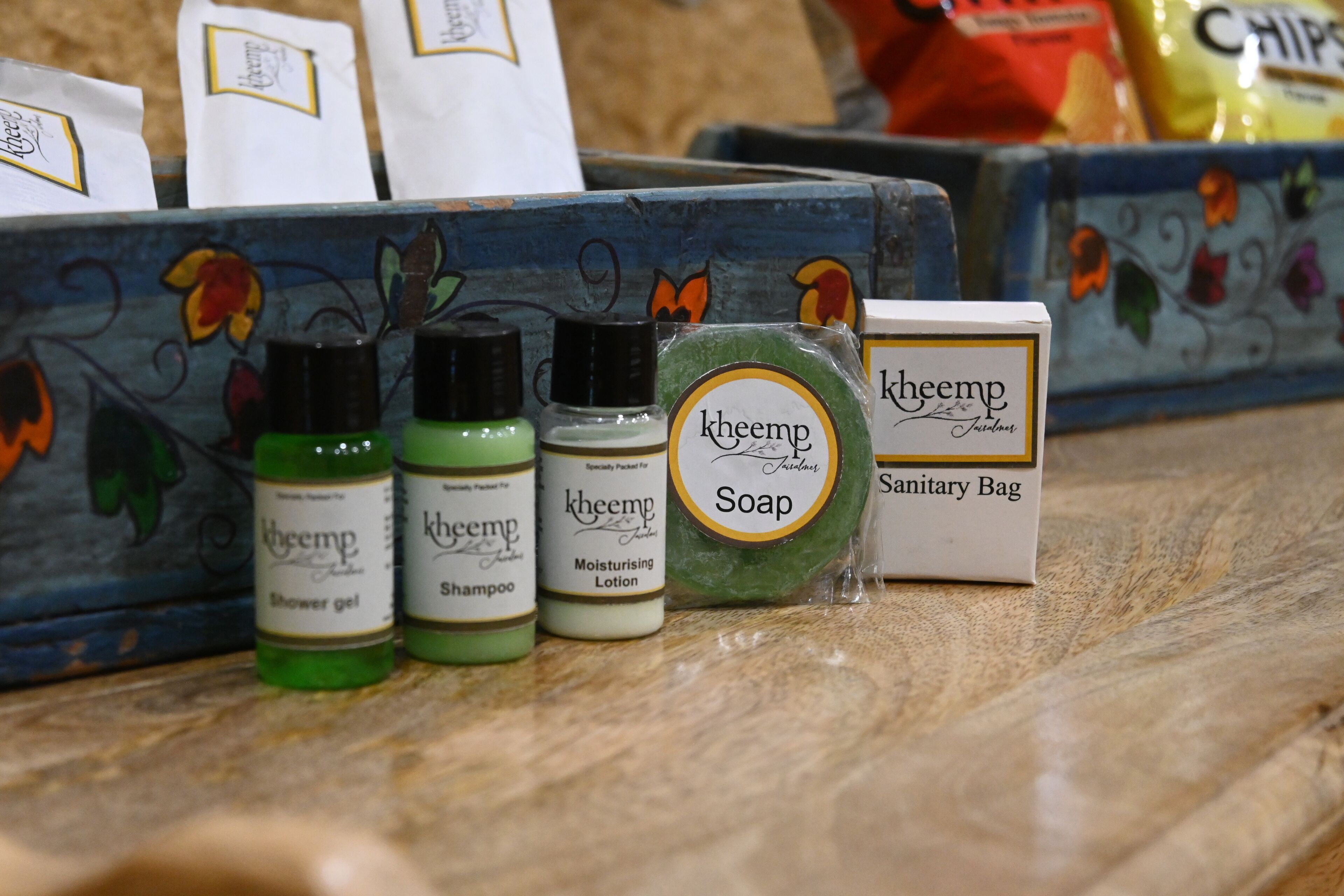 A display of various Kheemp products including shower gel, shampoo, moisturizing lotion, soap, and a sanitary bag.
