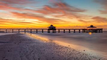 A pier with two structures at the end, extending over a calm beach.