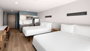 Hotellihuone, jossa on kaksi sänkyä, pieni keittiö, työpöytä ja tuoli.