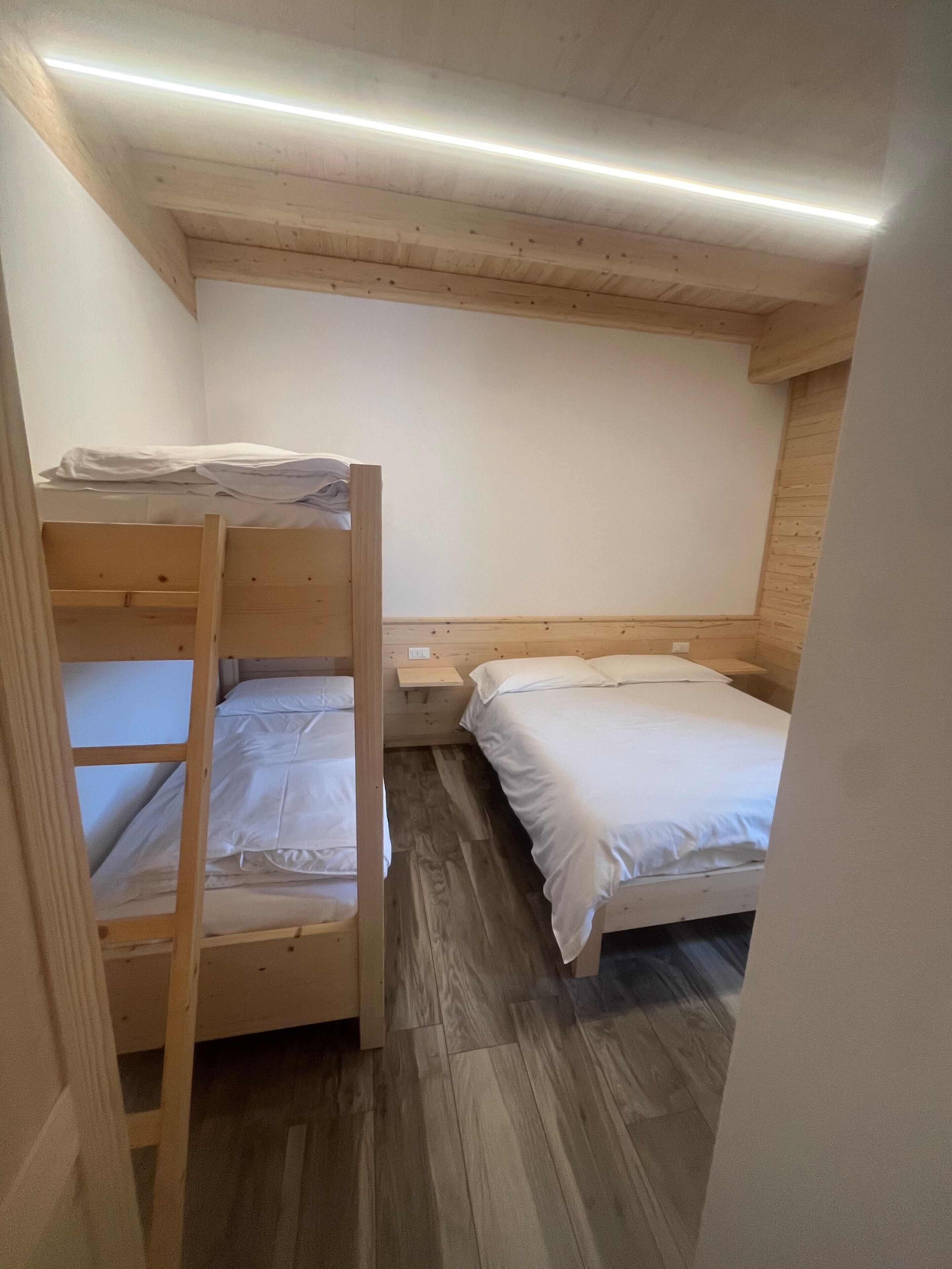 A small, compact room with a bunk bed and a single bed, wooden walls, and a sloped ceiling.