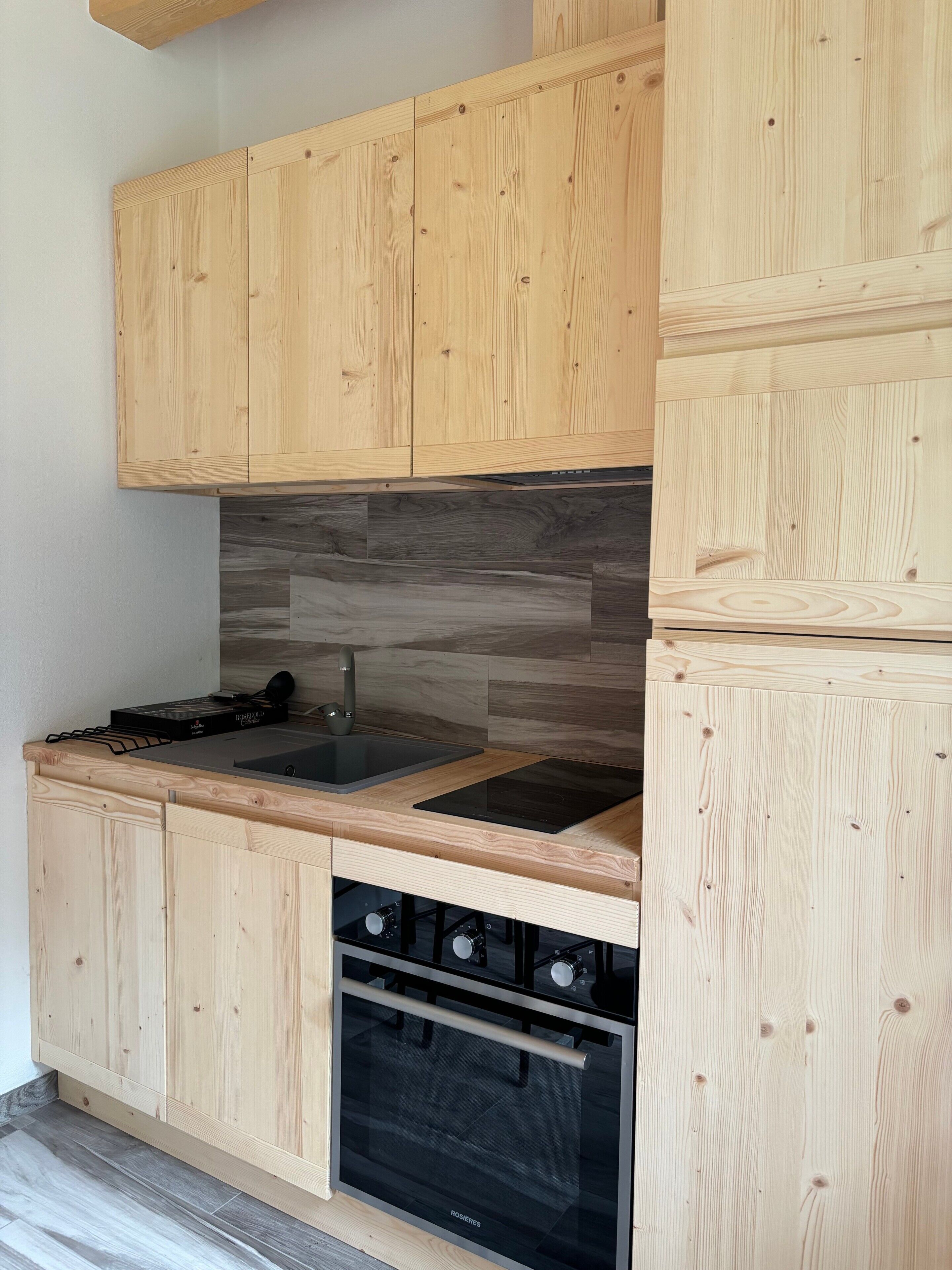 Une cuisine avec des meubles de rangement en bois, un plan de travail noir, un évier, une cuisinière et un four.
