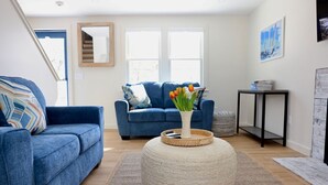 Een moderne woonkamer met een blauwe bank, een rond poef en een vaas met tulpen.