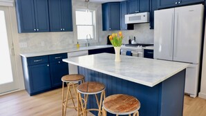Een moderne keuken met donkerblauwe kastjes, een wit marmeren eiland en houten krukken.