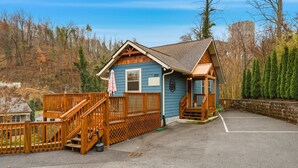 Eine kleine Holzhütte mit einer Holzterrasse, einer Veranda und einem Parkplatz.