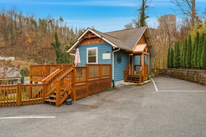 Eine kleine Holzhütte mit einer Holzterrasse, einer Veranda und einem Parkplatz.