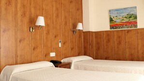 A hotel room with two beds, wooden panel walls, a painting, and an air conditioning unit. - Hostal Real (San Juan del Puerto)