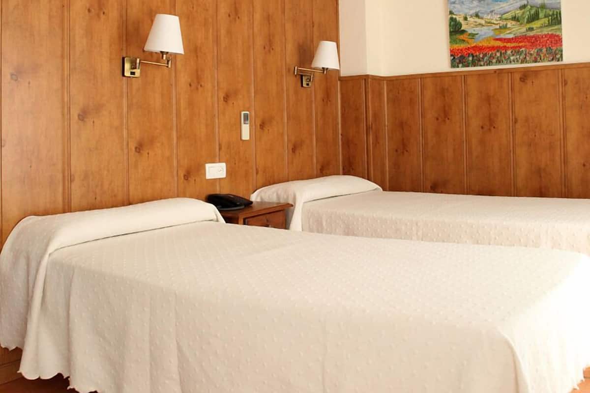Hotellihuone, jossa on kaksi sänkyä, puupaneloidut seinät, taulu ja ilmastointilaite.