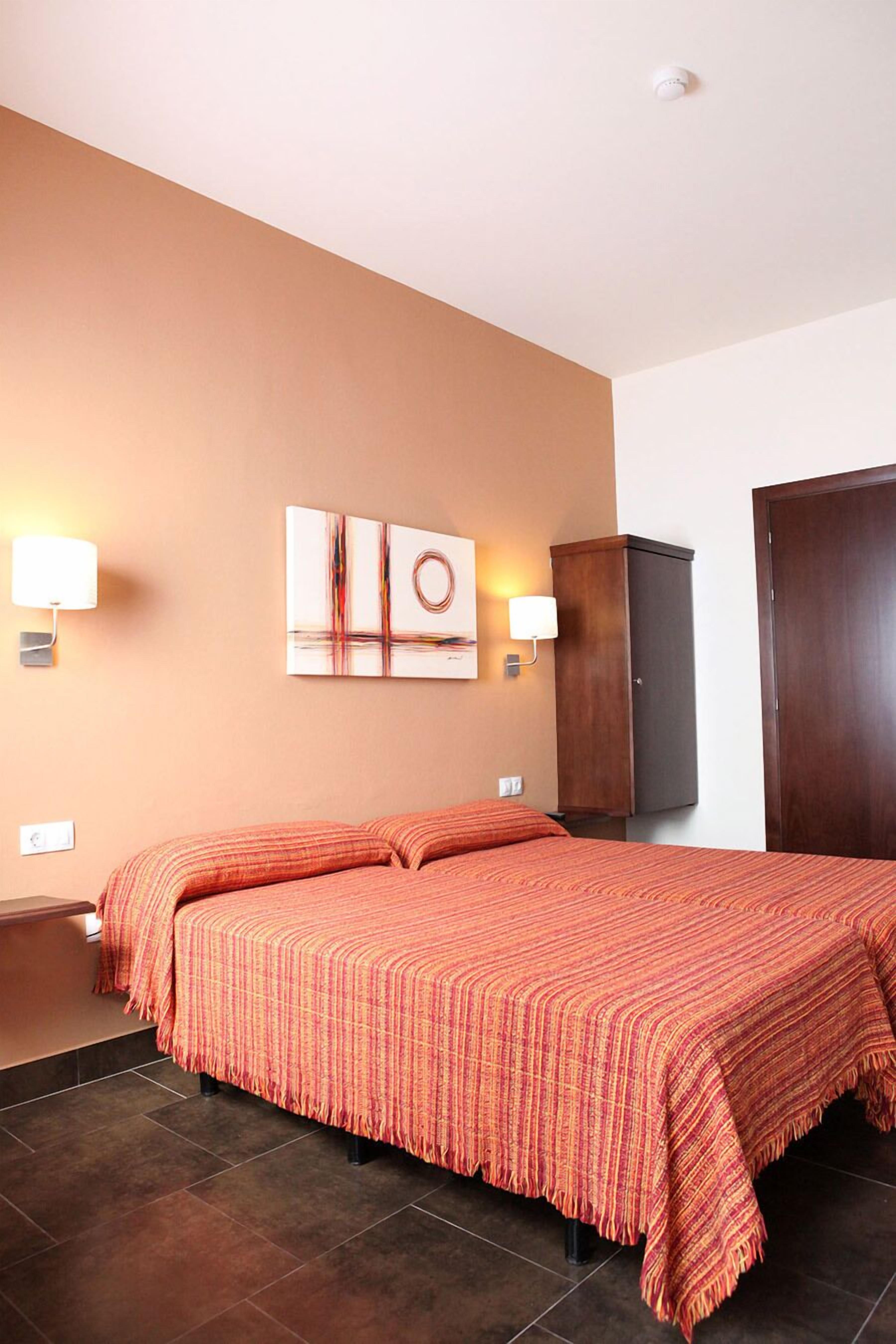 A hotel room with a large bed, two wall-mounted lamps, a wooden wardrobe, and a door.