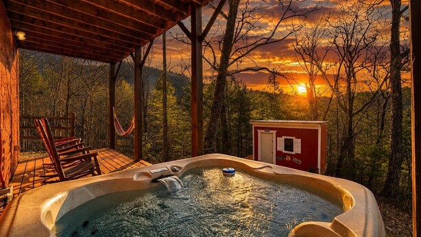 Uma banheira de hidromassagem com deck de madeira e um edifício vermelho numa área arborizada.