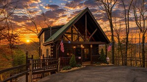 Uma cabana de tronco com varanda, bandeiras americanas e vista para o pôr do sol.