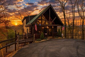Eine Holzhütte mit Veranda, amerikanischen Flaggen und Blick auf den Sonnenuntergang.