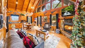 Interior acolhedor de uma cabana com área de jantar, lareira e árvore de Natal.