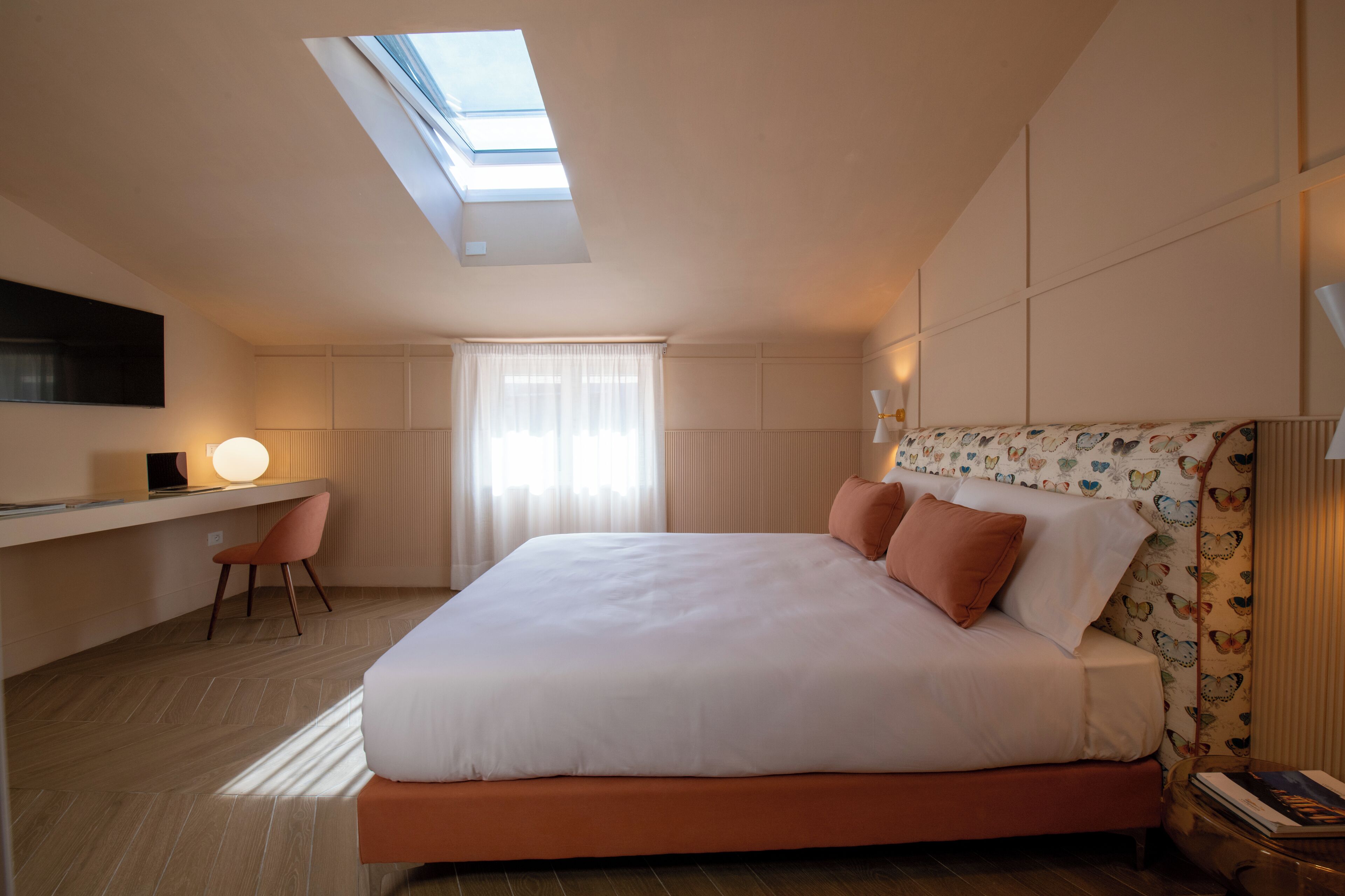 Une chambre à coucher moderne avec une lucarne, un lit avec une literie blanche, un bureau avec une chaise et une tête de lit à motifs.