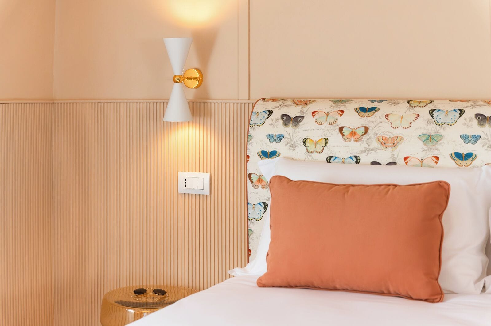 A hotel room with a bed, a nightstand, a wall-mounted light fixture, and a power outlet.