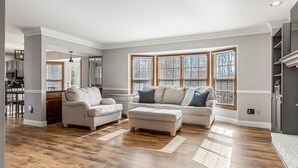 A spacious living room with hardwood flooring, two sofas, a coffee table, and large windows with blinds. - 5BR Group Retreat | Hot Tub, Deck & Workspace (Saint Charles)