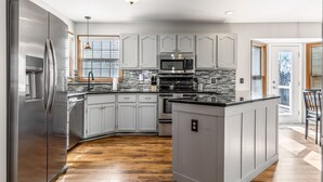 A modern kitchen with a stainless steel refrigerator, a microwave, and an island with a sink. - 5BR Group Retreat | Hot Tub, Deck & Workspace (Saint Charles)