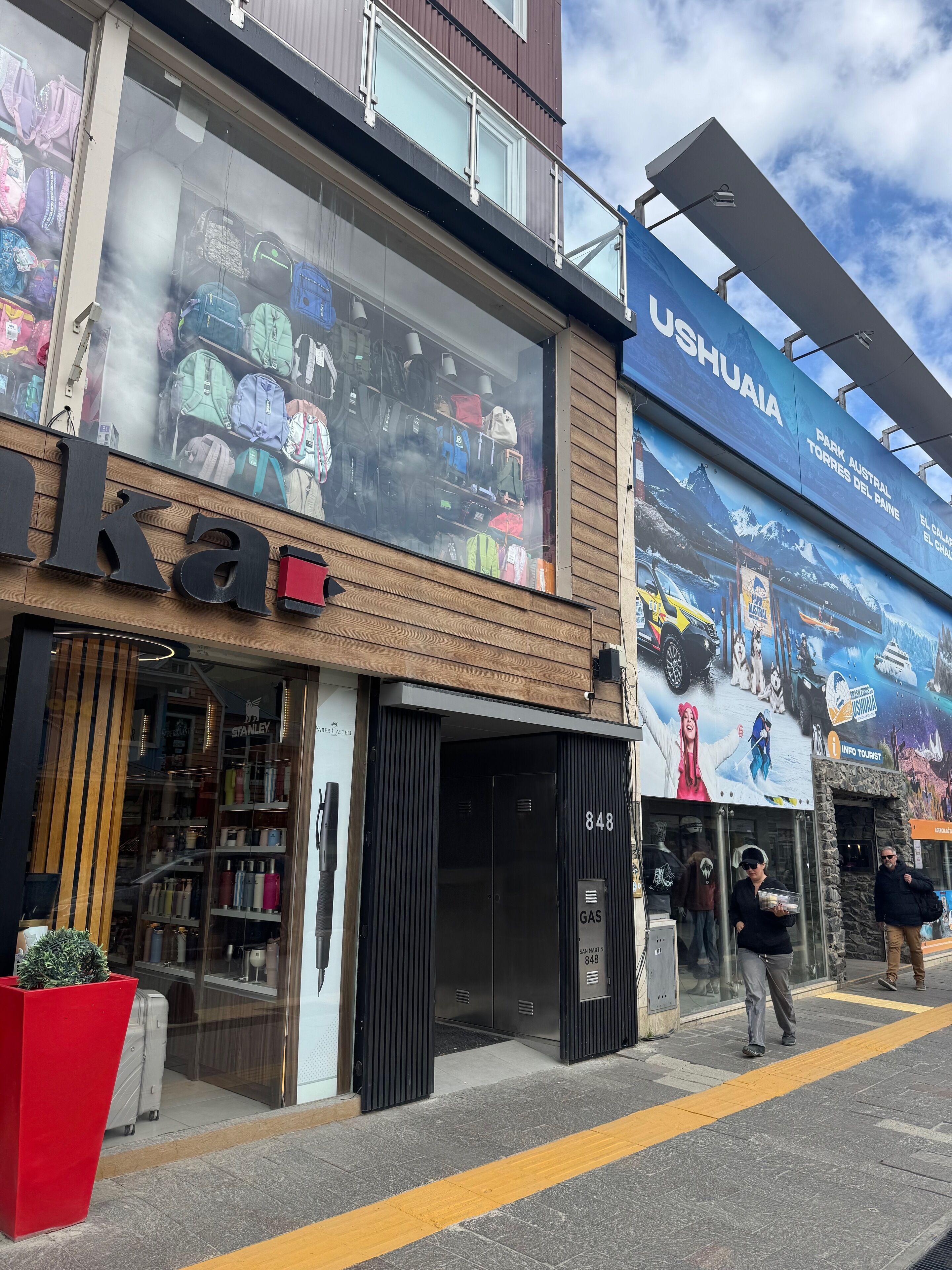 Fachada de loja com malas e acessórios de viagem, nome da loja visível e um grande anúncio ao ar livre para um parque.