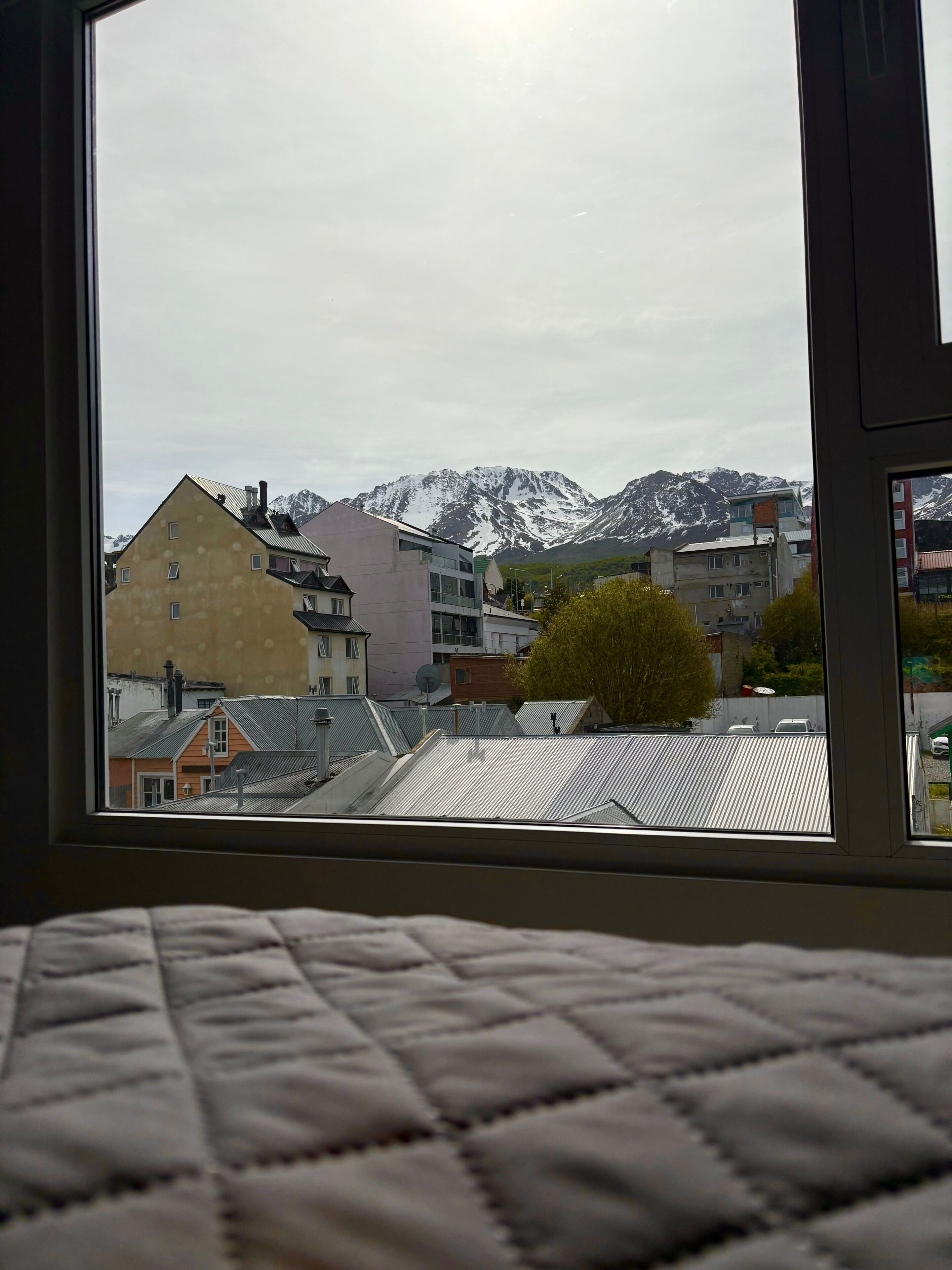 Une pièce dotée d’une grande fenêtre donnant sur un paysage urbain, avec des bâtiments et des montagnes enneigées en arrière-plan.