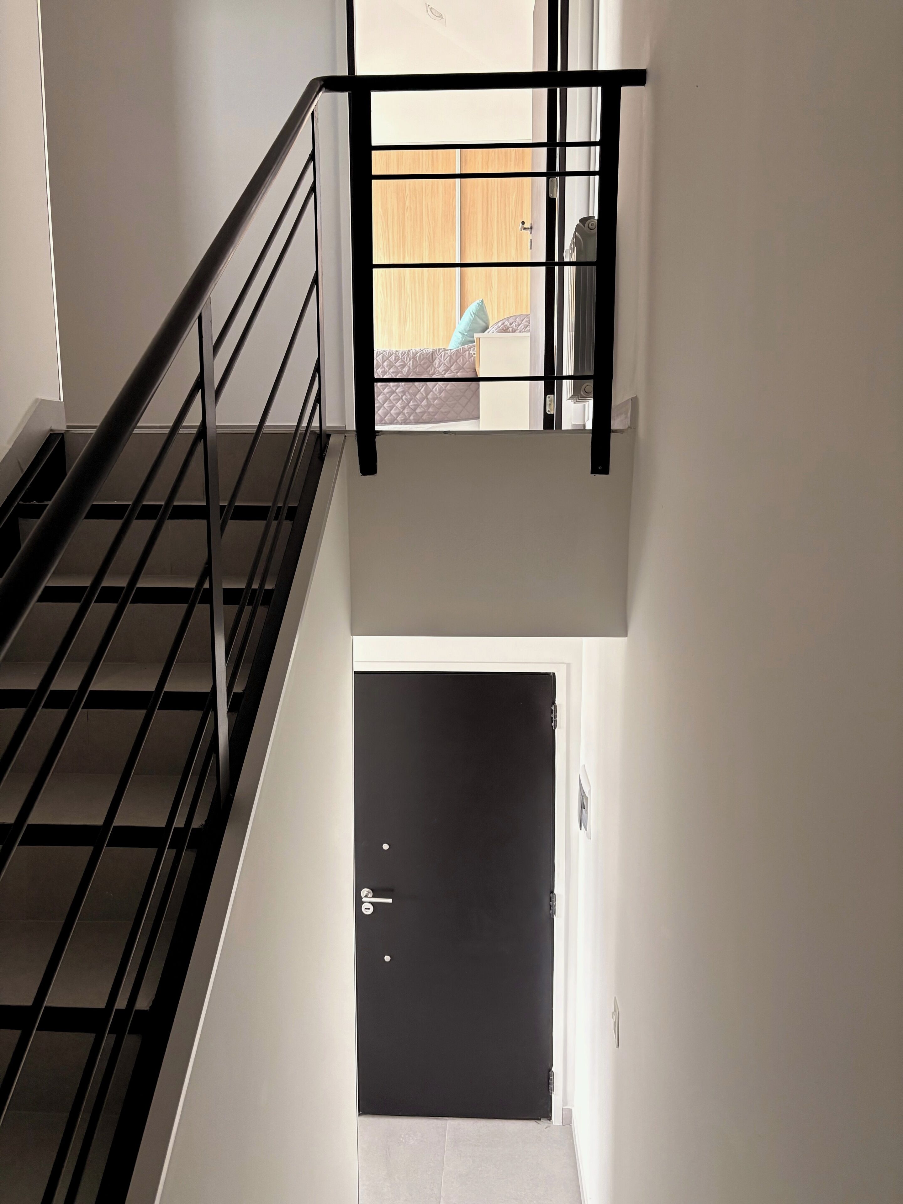 A staircase with a black metal railing leading to a bedroom with a wooden door.