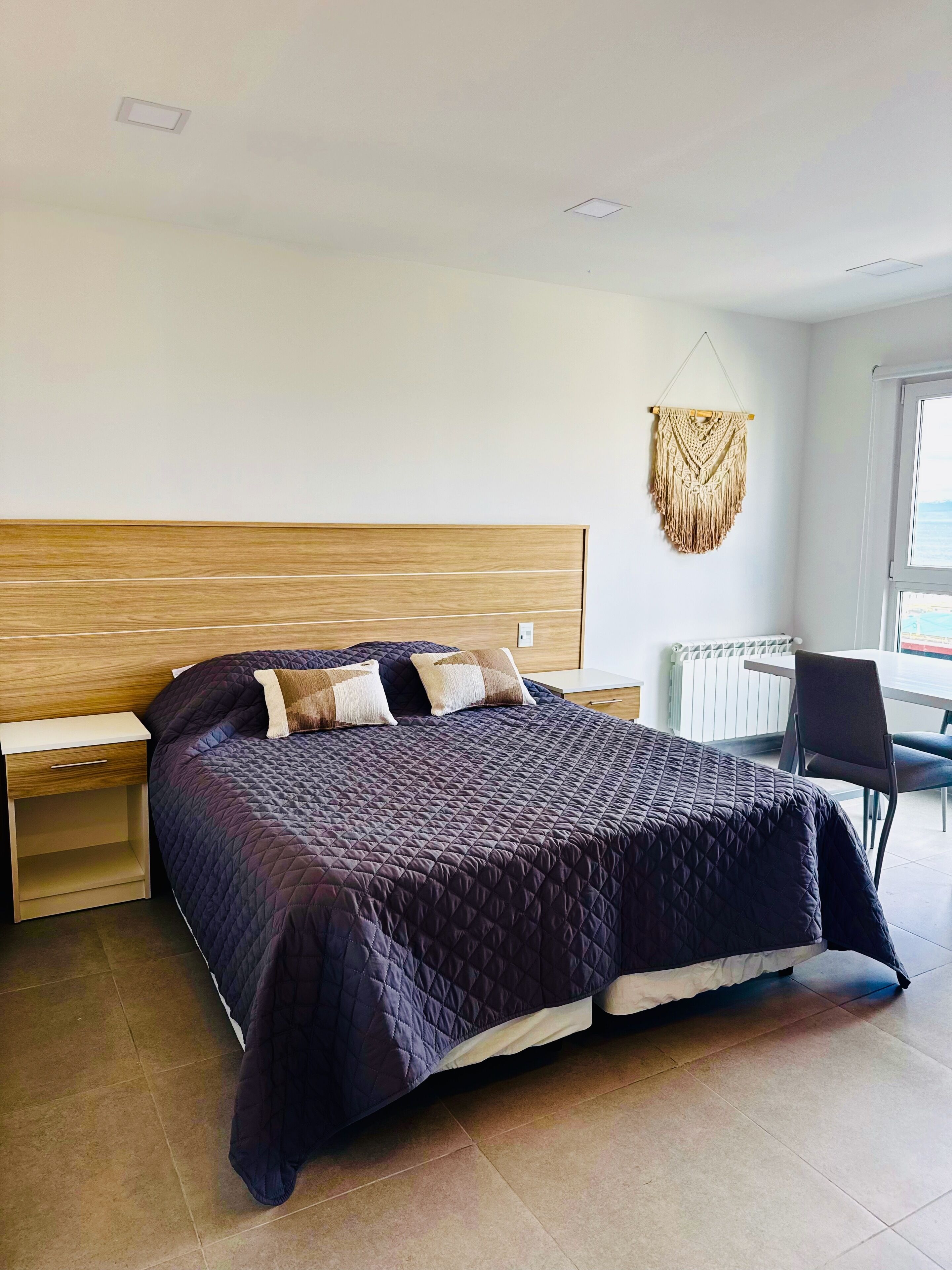 A bedroom with a bed, bedside tables, a chair, and a macrame wall hanging.