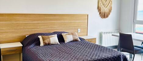 A bedroom with a bed, bedside tables, a chair, and a macrame wall hanging.