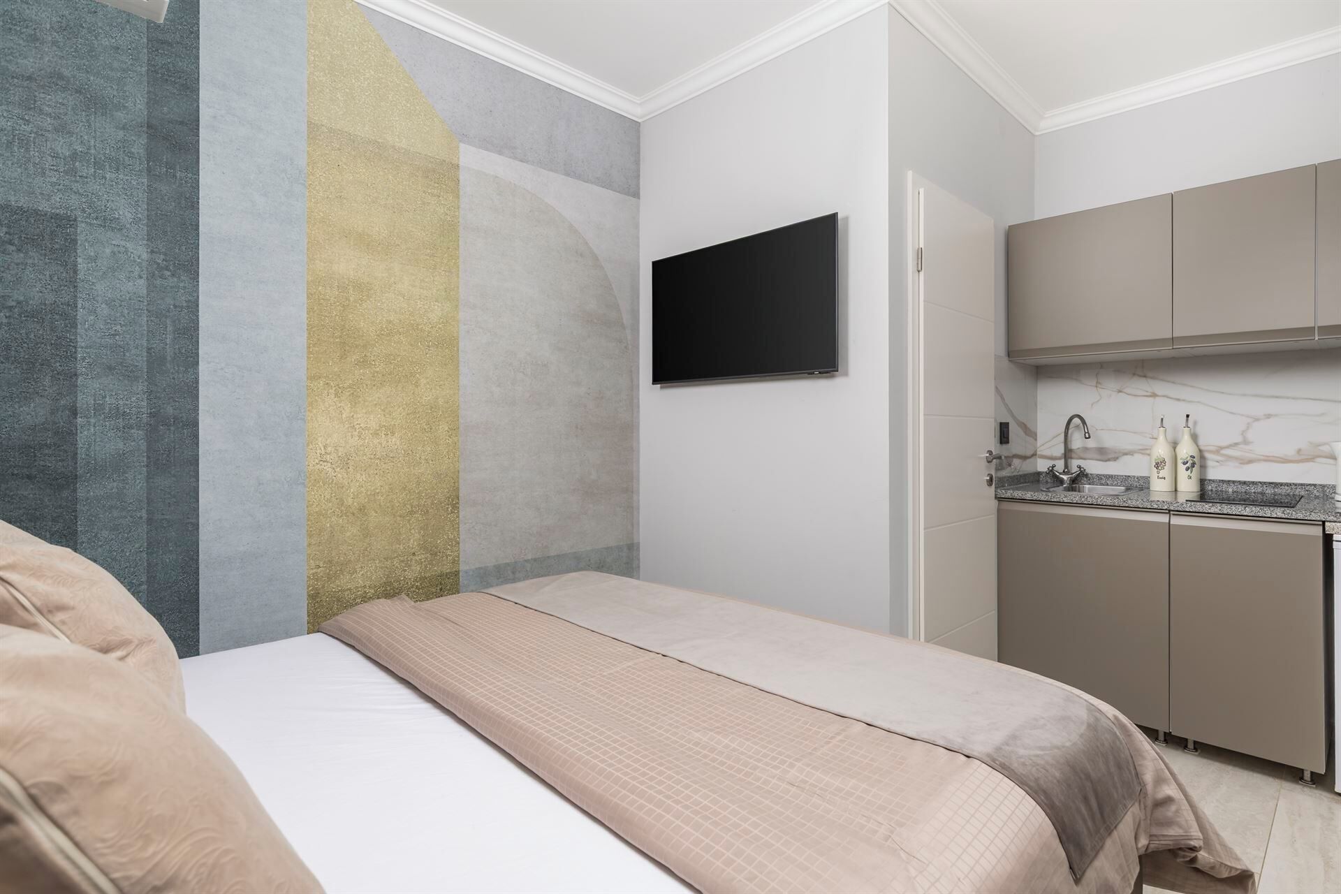 Ein Schlafzimmer mit einem Bett, einem an der Wand befestigten Fernseher und einer Küchenzeile mit Schränken und einem Spülbecken.