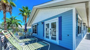 A blue building with a covered deck, outdoor seating, and palm trees. - Steps to Manatee Beach, Pool, and Private Sun Deck (Holmes Beach)
