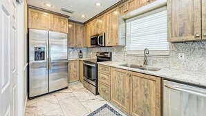 A kitchen with wooden cabinets, stainless steel appliances, a granite countertop, and a window with blinds. - Steps to Manatee Beach, Pool, and Private Sun Deck (Holmes Beach)