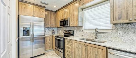 A kitchen with wooden cabinets, stainless steel appliances, a granite countertop, and a window with blinds.