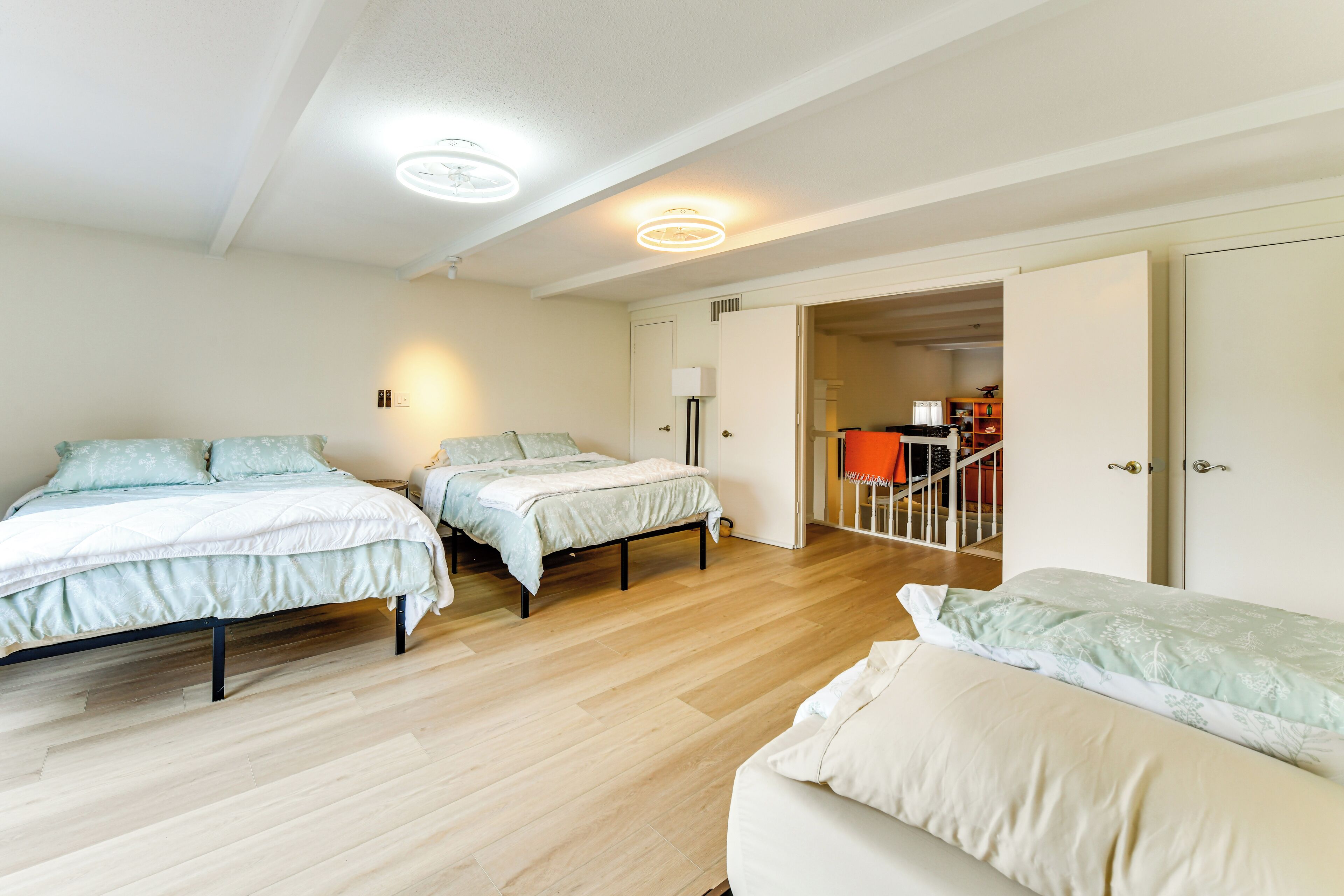 A bedroom with three beds, a wooden floor, and a door leading to another room.