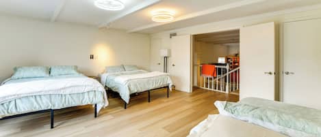 A bedroom with three beds, a wooden floor, and a door leading to another room.