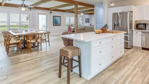 A spacious kitchen with a large island, wooden flooring, white cabinetry, and modern appliances. - Jensen Beach Indian River Waterfront Retreat (Jensen Beach)