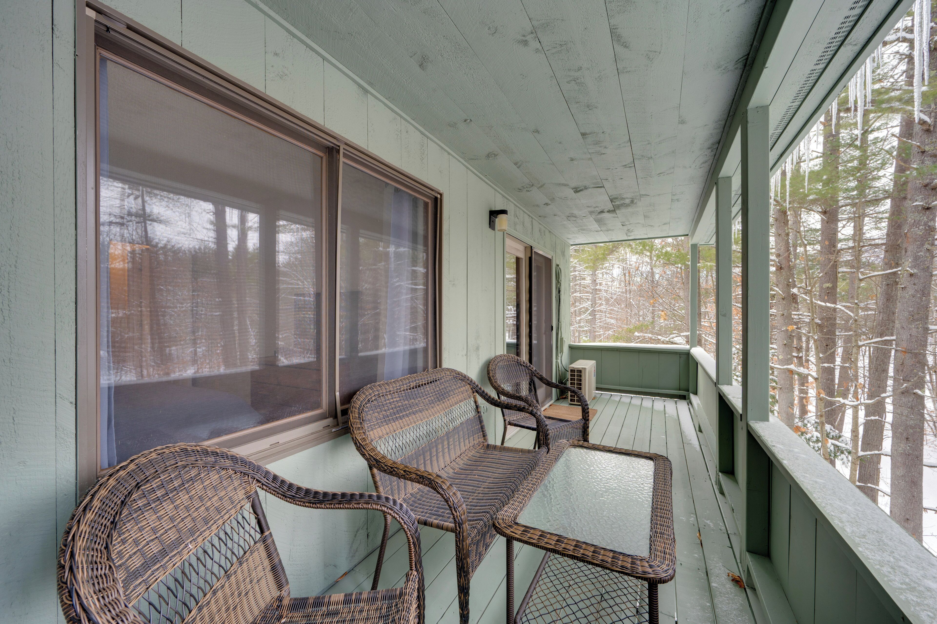A covered porch with wicker furniture and large windows.