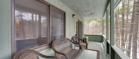 A covered porch with wicker furniture and large windows.