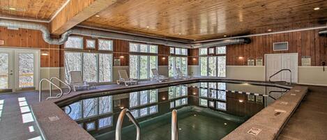 Una piscina interior con techo de madera, ventanas amplias y sillones de descanso.