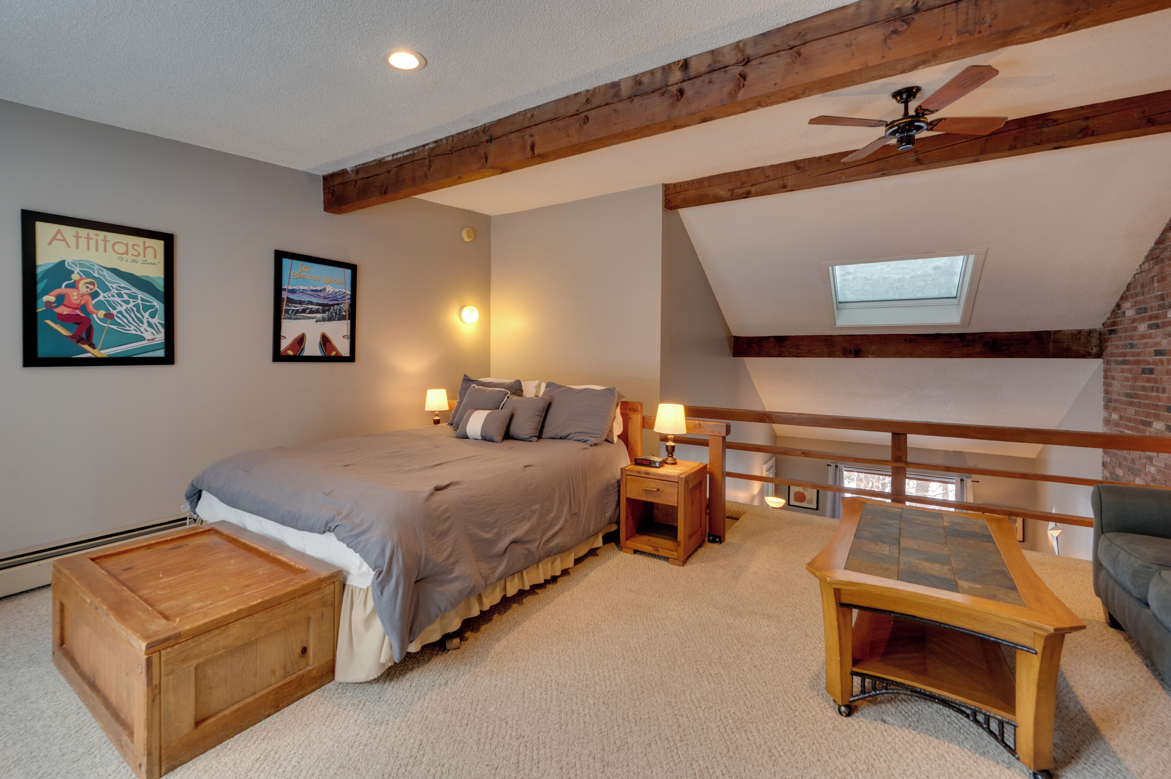 A bedroom with a bed, bedside tables, a wooden nightstand, a desk, a ceiling fan, and a window.