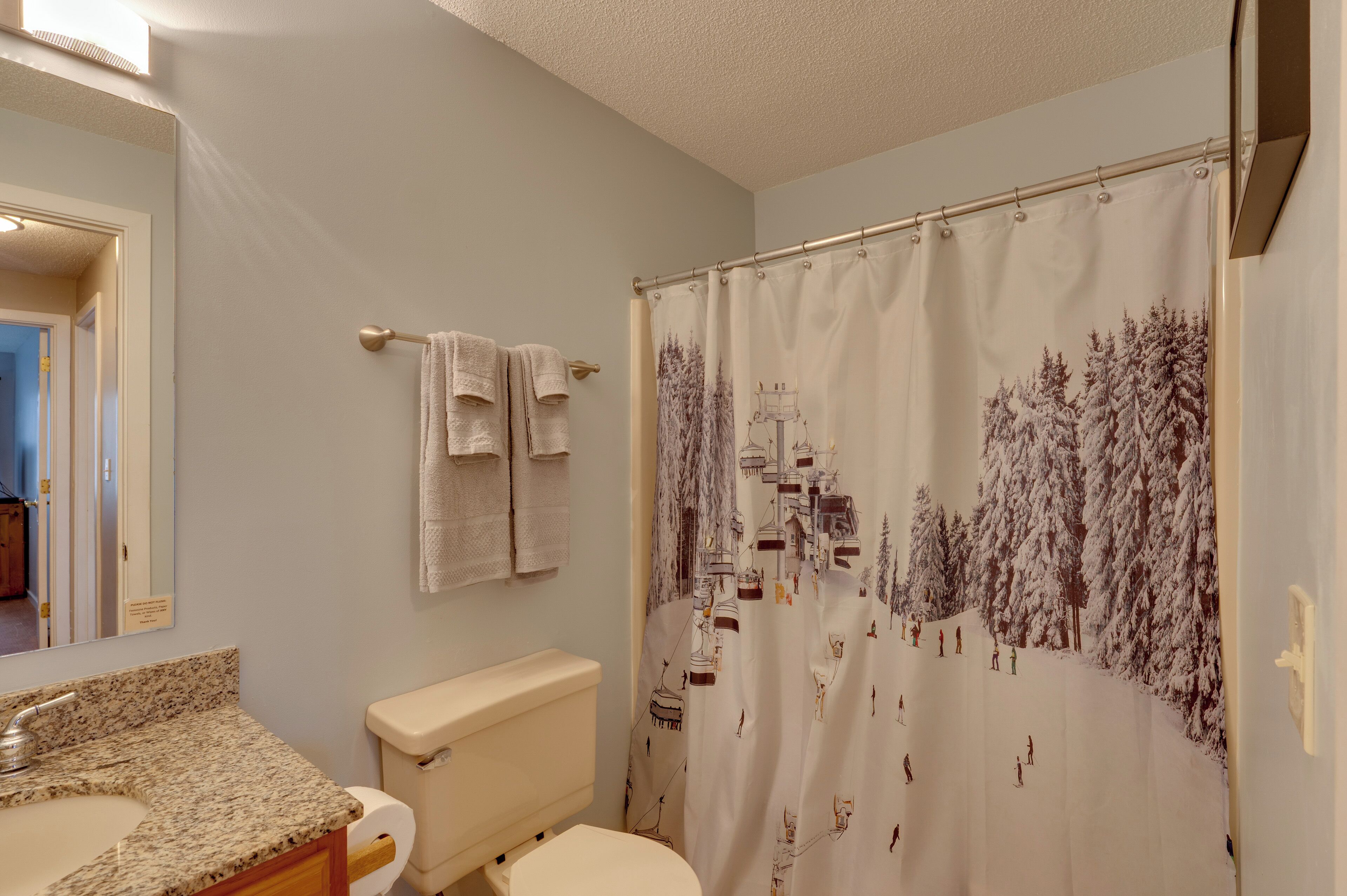 Un baño con inodoro, lavamanos y cortina de ducha con motivo invernal.